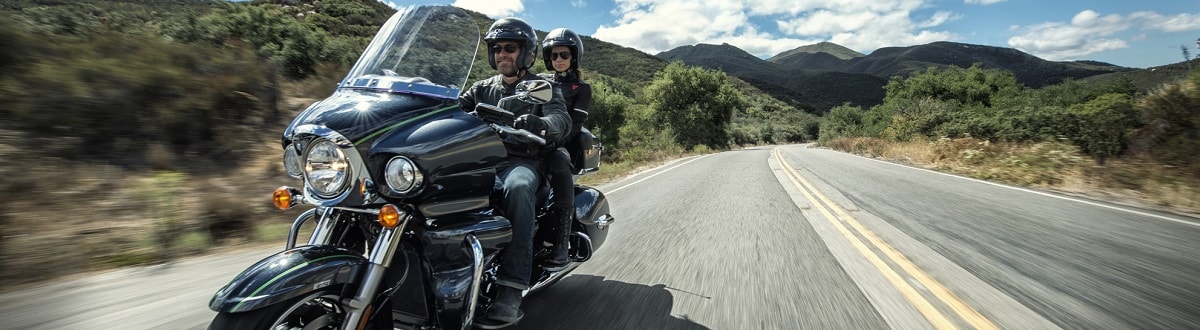 A man and woman in protective gear both riding a Harley-Davidson® CVO® motorcycle on a desert highway.
