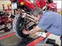 A man working on the back tire of a red motorcycle in a repair shop.